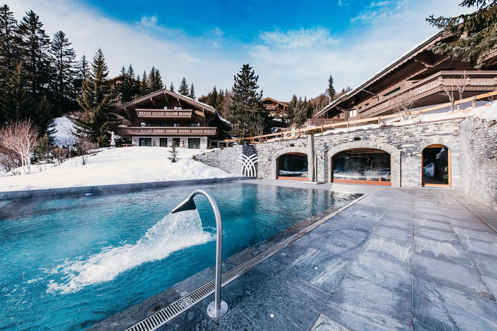 Heated outdoor pool and stone arches of Chalet Christiana in the snow, Crans-Montana